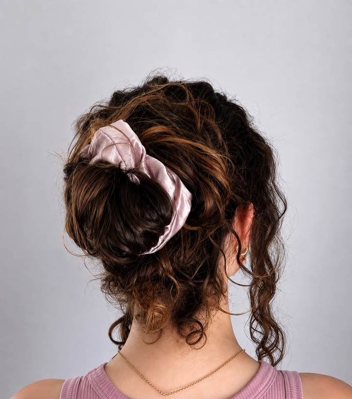 Back view of a woman wearing a Lotus pink 22 momme mulberry silk scrunchie in a curly bun hairstyle